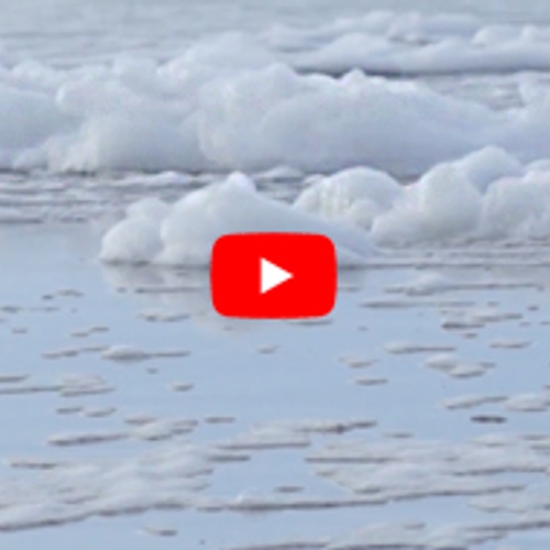 Schuimkoppen waaien over het strand